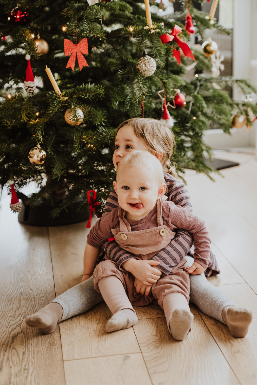 Zwei kleine Kinder sitzen vor dem Weihnachtsbaum.