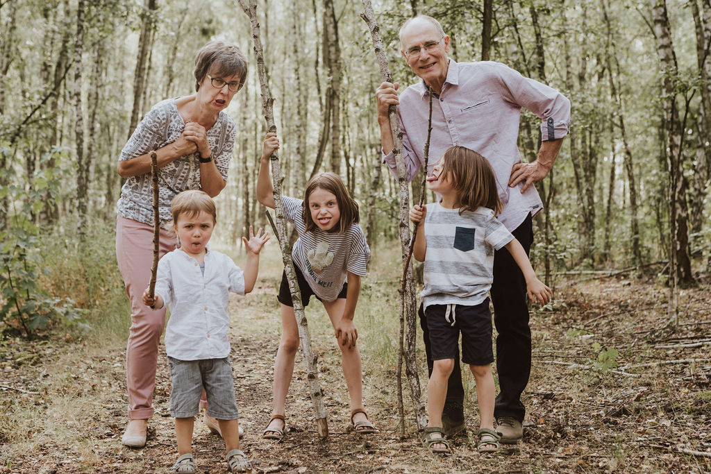 Ein Mann und eine Frau stehen mit drei Kindern im Wald und halten Stöcke.