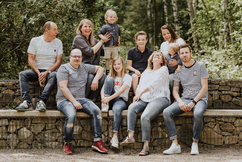 Eine Gruppe von Menschen die im Wald auf einer Steinwand sitzen und für ein Familienfoto posieren.