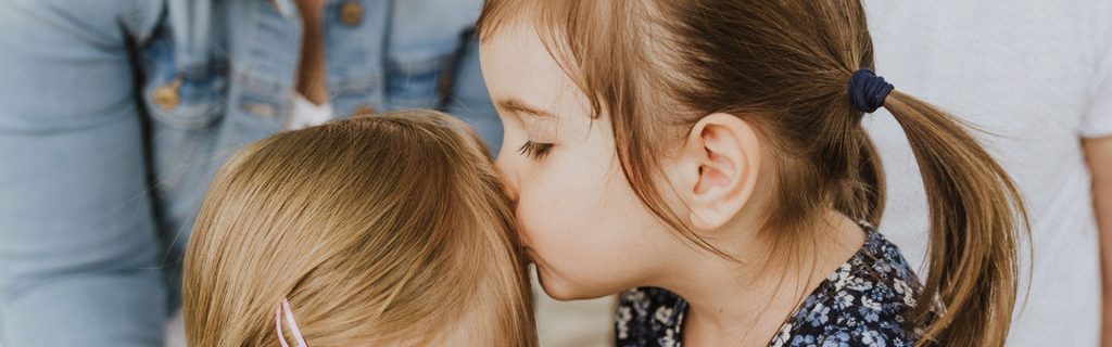 Ein kleines Mädchen gibt einen Kuss auf die Stirn einen anderem Mädchen.