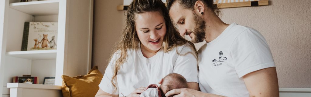 Junge Eltern halten ihr neugeborenes Baby und schauen es liebevoll an