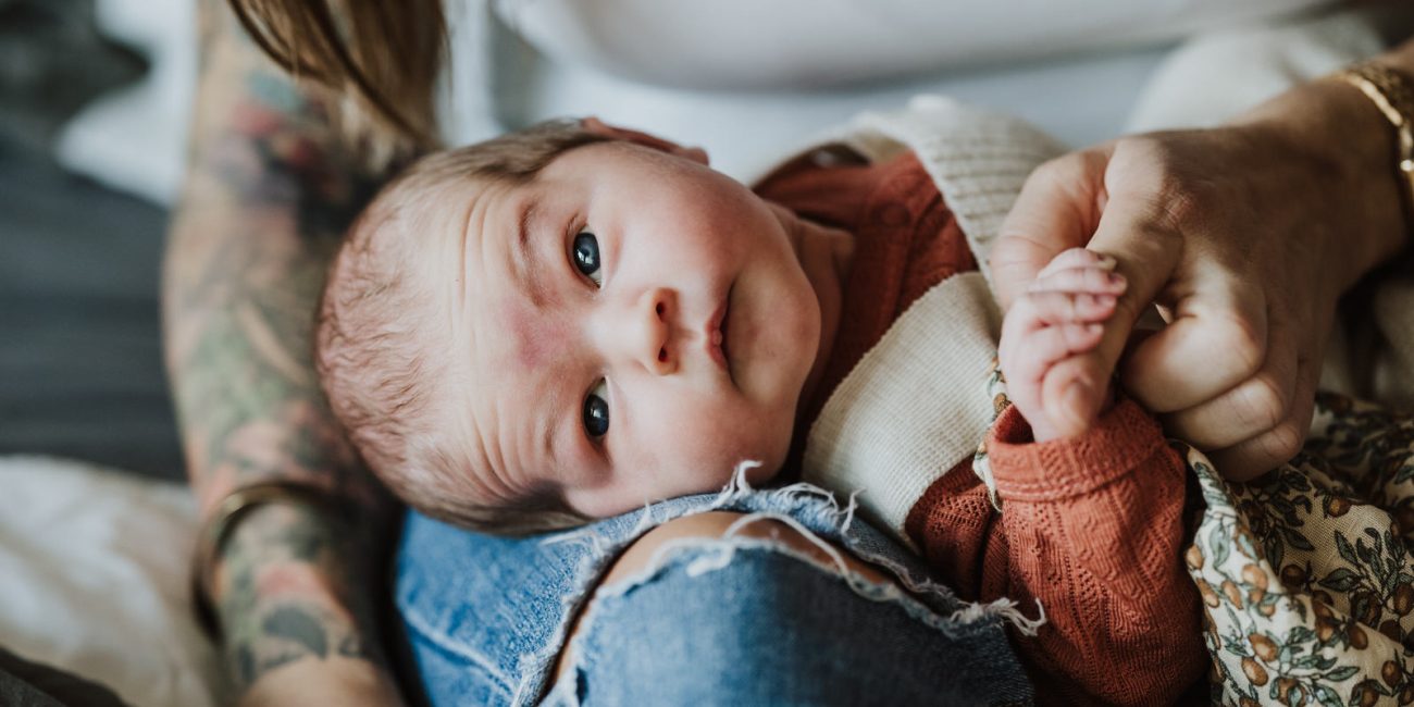 Das neugeborenes Baby schaut aufmerksam in die Kamera und hält Mamas Finger fest