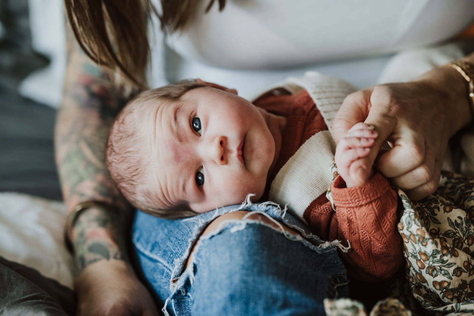 Das neugeborenes Baby schaut aufmerksam in die Kamera und hält Mamas Finger fest