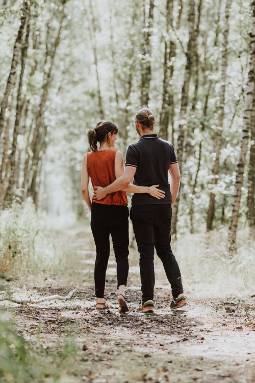 Ein Mann und eine Frau spazieren umarmt durch einen Wald.