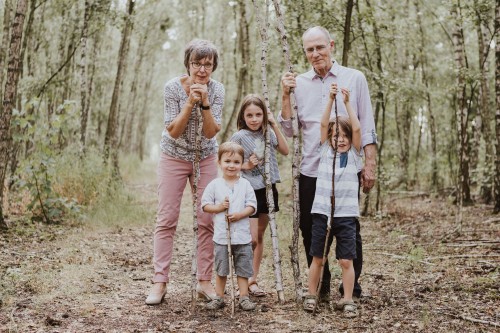 Eine ältere Frau und ein älterer Mann stehen mitten im Wald mit drei kleinen Kindern.