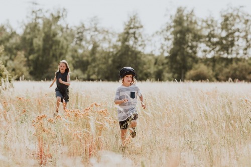 Zwei kleine Kinder laufen durch eine Wiese.