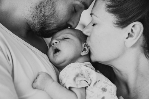 Ein Mann und einer Frau küssen ein kleines Baby.