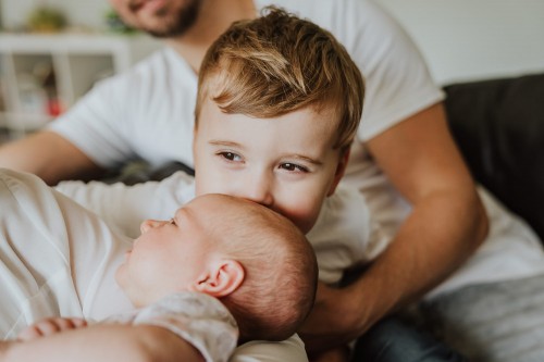 Ein kleiner Junge küsst ein Baby auf dem Kopf.