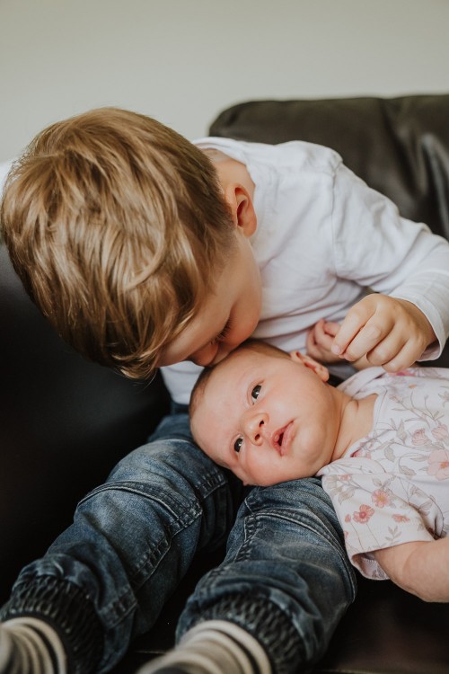 Ein kleiner Junge küsst ein Baby auf dem Kopf.