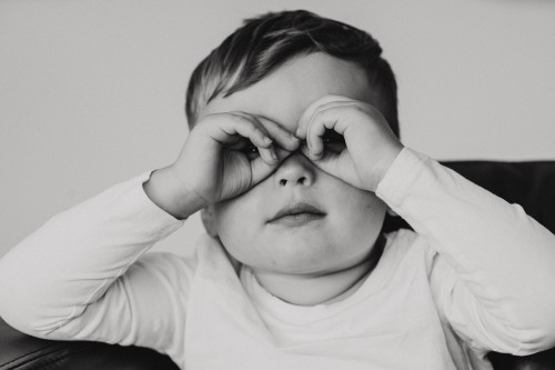 Ein schwarz-weiß Foto von einem kleinen Jungen der sich die Hände vor den Augen hält.