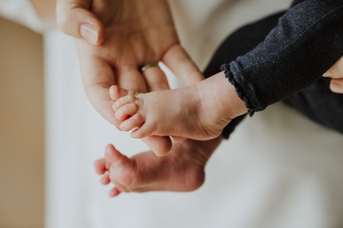 Eine große Hand hält kleine Baby Füße.