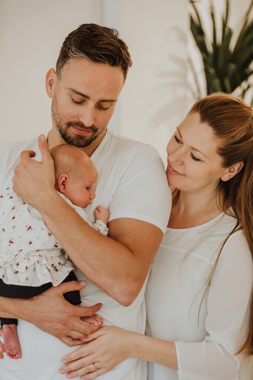 Ein Mann mit einem Kind auf dem Arm wird von einer Frau umarmt.