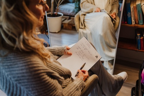 Eine Frau sitzt vor einem Spiegel und hält ein Notizbuch.