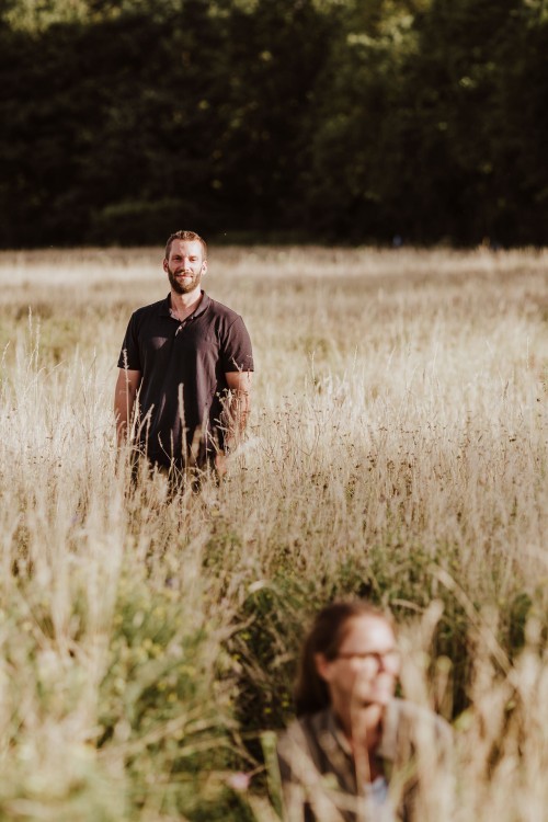 Ein Mann steht auf einer Wiese und schaut zu seiner Frau.