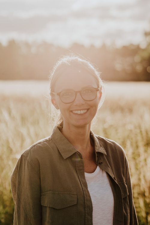 Eine Frau steht mitten auf einer Wiese im Sonnenuntergangslicht.