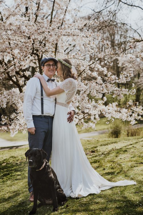 Farbfoto Brautpaar umgeben von Kirschblüten mit Hund