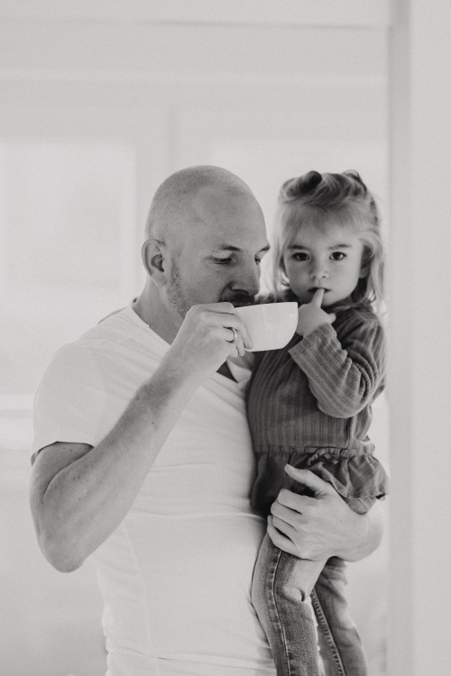 Ein Mann hält ein kleines Mädchen auf dem Arm und trinkt dabei Kaffee.