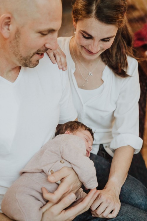 Ein Mann hält ein Baby auf dem Schoß und eine Frau sitzt hinter ihn.