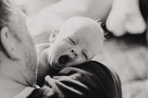 Ein kleines Baby gähnt bei einem Mann auf dem Arm.