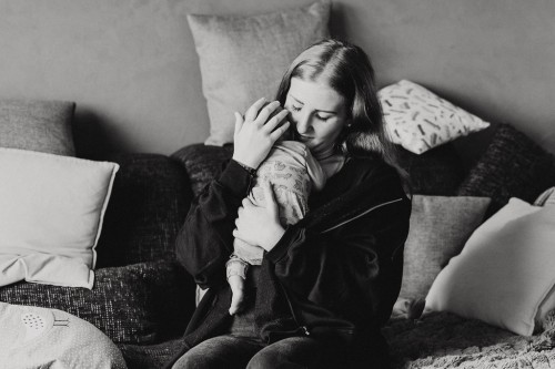 Eine Frau sitzt auf einer Couch und hält ein kleines Baby an ihrer Brust.