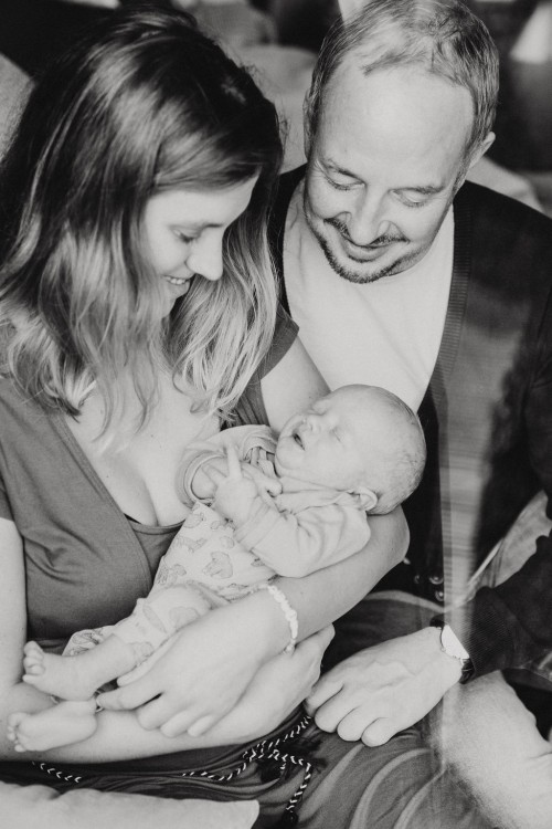 Eine Frau mit einem Kind auf dem Arm und ein Mann sitzen auf einer Couch.