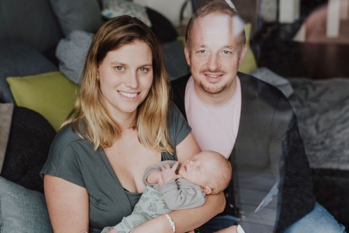 Eine Frau mit einem Kind auf dem Arm und ein Mann sitzen auf einer Couch.