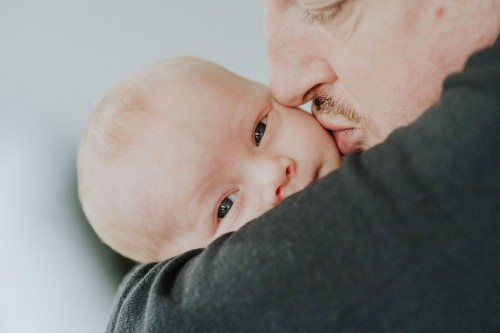 Ein kleines Baby bei einem Mann auf dem Arm bekommt einen Kuss auf die Wange.