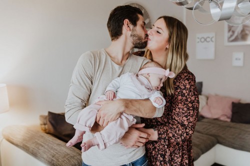 Ein Mann und eine Frau küssen sich und halten ein kleines Baby im Arm.