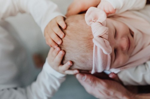 Kleine Hände streicheln das Baby am Kopf.