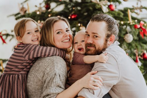 Eine Frau und ein Mann sitzen mit zwei kleinen Kindern vor einem Weihnachtsbaum.