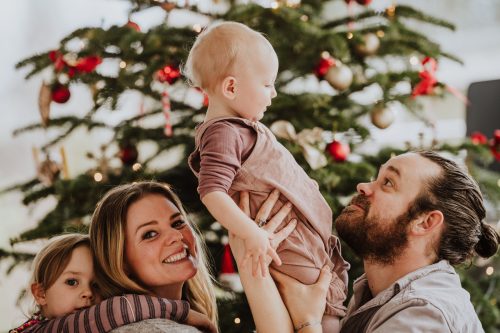 Eine Frau und ein Mann sitzen mit zwei kleinen Kindern vor einem Weihnachtsbaum.