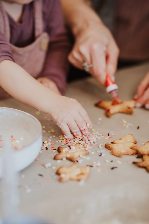 Ein Kind und ein Erwachsener dekorieren Weihnachtsplätzchen.