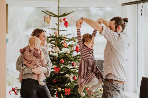 Eine Frau und ein Mann tanzen mit zwei kleinen Kindern vor einem Weihnachtsbaum.