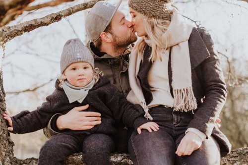 Eine Frau und ein Mann küssen sich und halten ein kleines Baby auf dem Schoß.