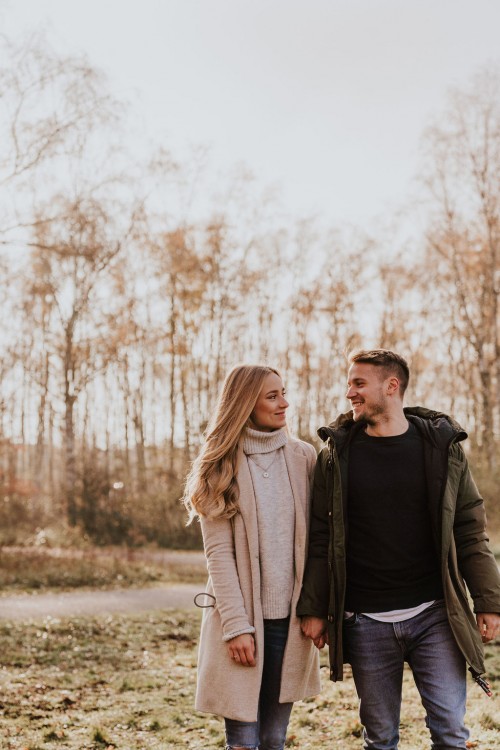 Eine Frau und ein Mann gehen händchenhaltend durch eine Wiese.