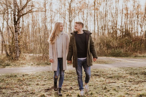 Eine Frau und ein Mann gehen händchenhaltend durch eine Wiese.