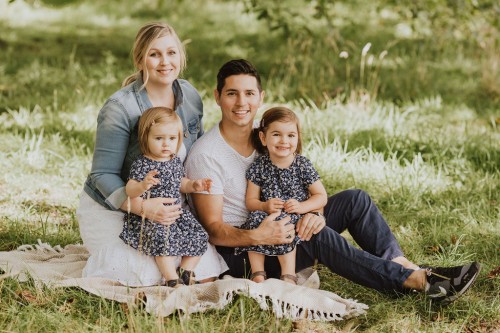 Eine Frau und ein Mann sitzen mit zwei kleinen Mädchen auf einer Wiese.