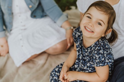 Ein kleines Mädchen, eine Frau und ein Mann sitzen auf einer Decke auf einer Wiese.