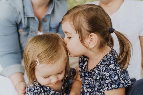 Ein kleines Mädchen gibt einen Kuss auf die Stirn einen anderem Mädchen.