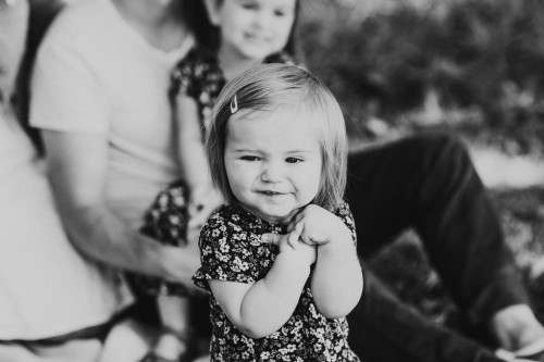 Ein kleines Mädchen sitzt auf dem Boden, hinter ihr sitzt eine Frau und hält ein kleines Mädchen auf dem Schoß.