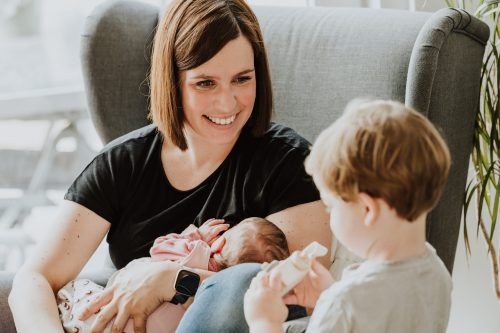 Eine Frau hält ein kleines Baby und schaut zu ihren kleinen Sohn hin.