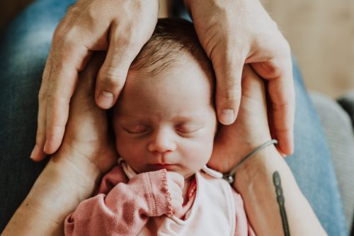 Ein kleines Baby liegt auf den Händen von den Eltern.