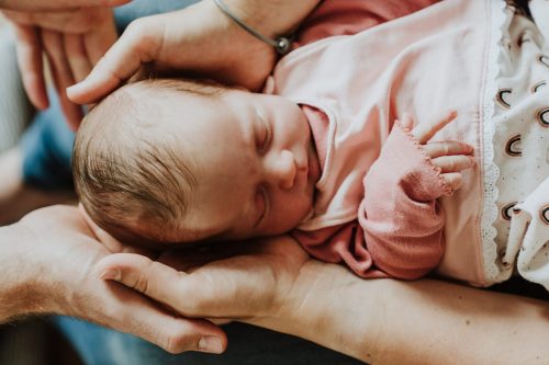 Ein kleines Baby liegt auf den Händen von den Eltern.
