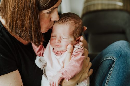 Eine Frau küsst ein kleines Baby am Kopf.