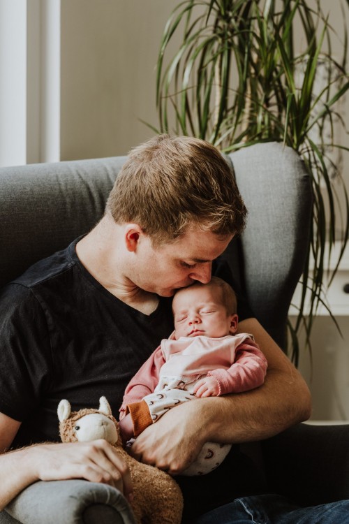 Ein Mann hält ein kleines Baby auf dem Arm und küsst es auf dem Kopf.