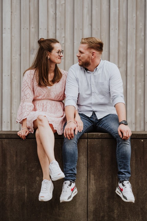 Eine Frau und ein Mann sitzen vor einer Holzwand.