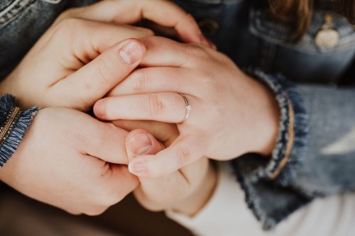 Eine Hand mit einem Ring wird durch andere Hände festgehalten.