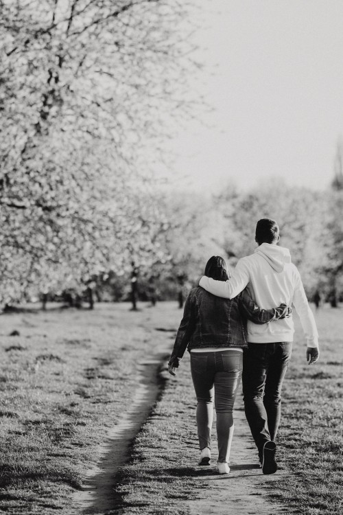 Eine Frau und ein Mann gehen umarmt einen Feldweg entlang.