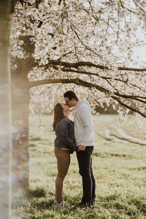 Eine Frau und ein Mann küssen sich vor einem Obstbaum.