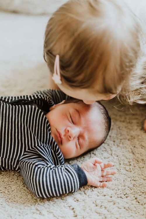 Ein kleines Baby wird von einem Kind am Kopf geküsst.